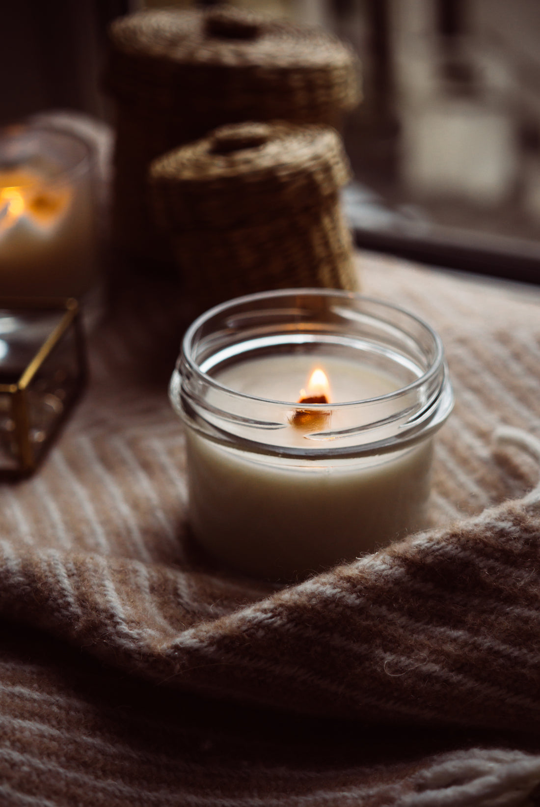 Close-up of a hand-poured candle with a wooden wick burning in a glass jar, warm glow